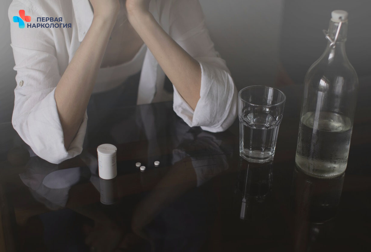 Человек сидит за столом с бутылкой, стаканом и таблетками